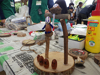 制作中と思われる木工工作。丸いコースターの縁に4どんぐりとエンピツ状小枝先端にマンガキャラクター