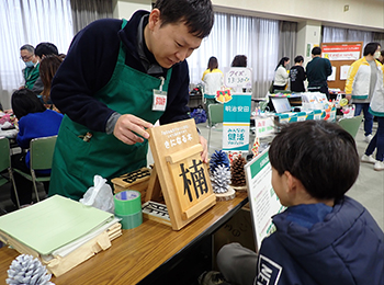 会場で木へんのつく漢字クイズ。左手黒ジャケット職員「楠」提示読みに挑戦する小学生